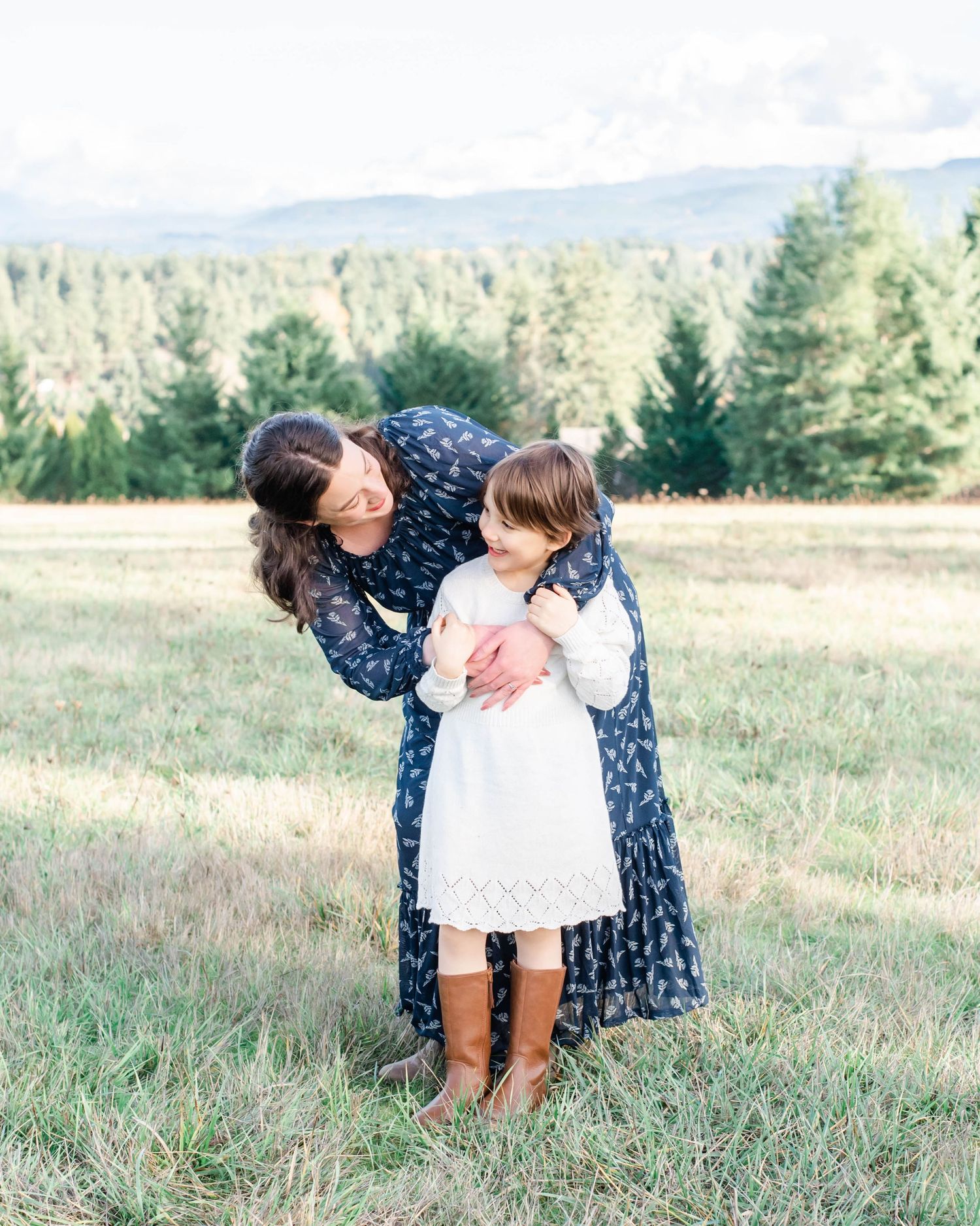 Affectionate moment captured in sunlit field with mountain backdrop.