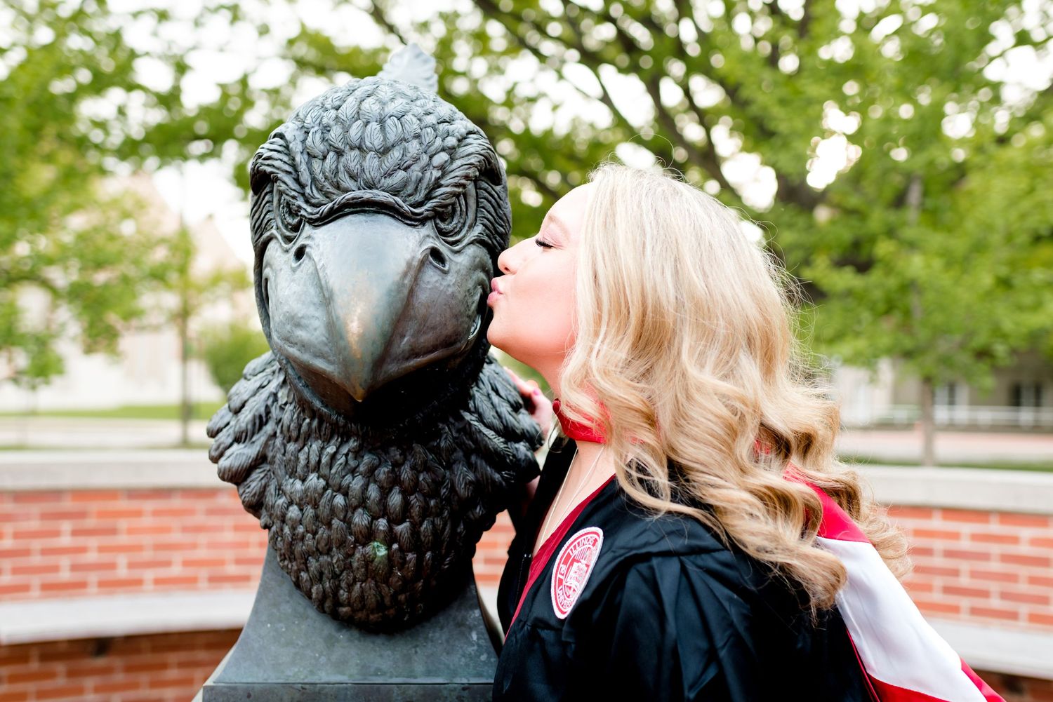 Illinois State University senior graduate kissing the Redbird statue during a cap and gown session by Julie Loy Photography