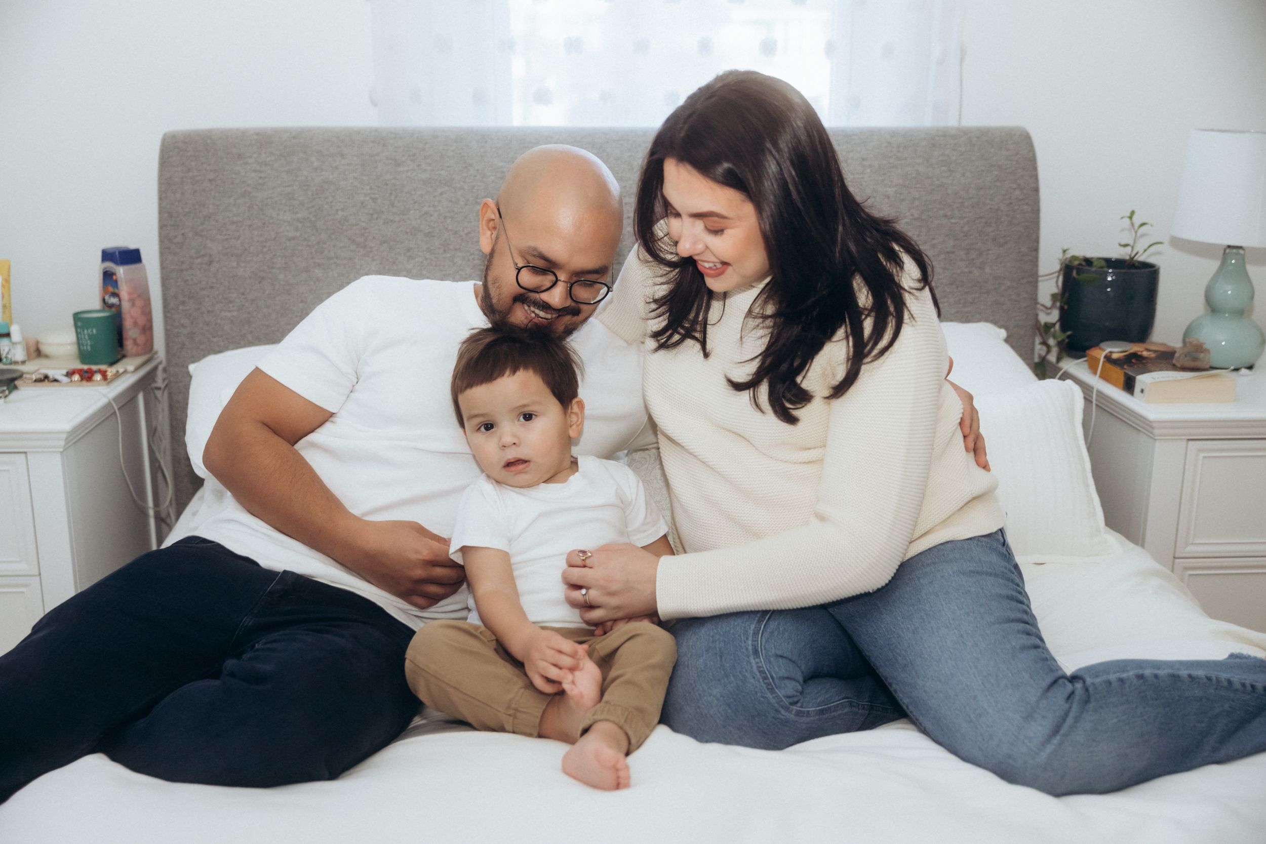 A family relaxing together on a gray couch in a cozy bedroom setting.