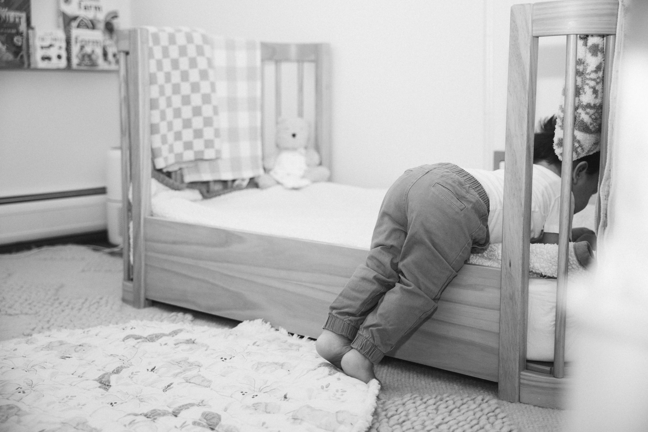 A child playfully climbing over a wooden bed frame in black and white.