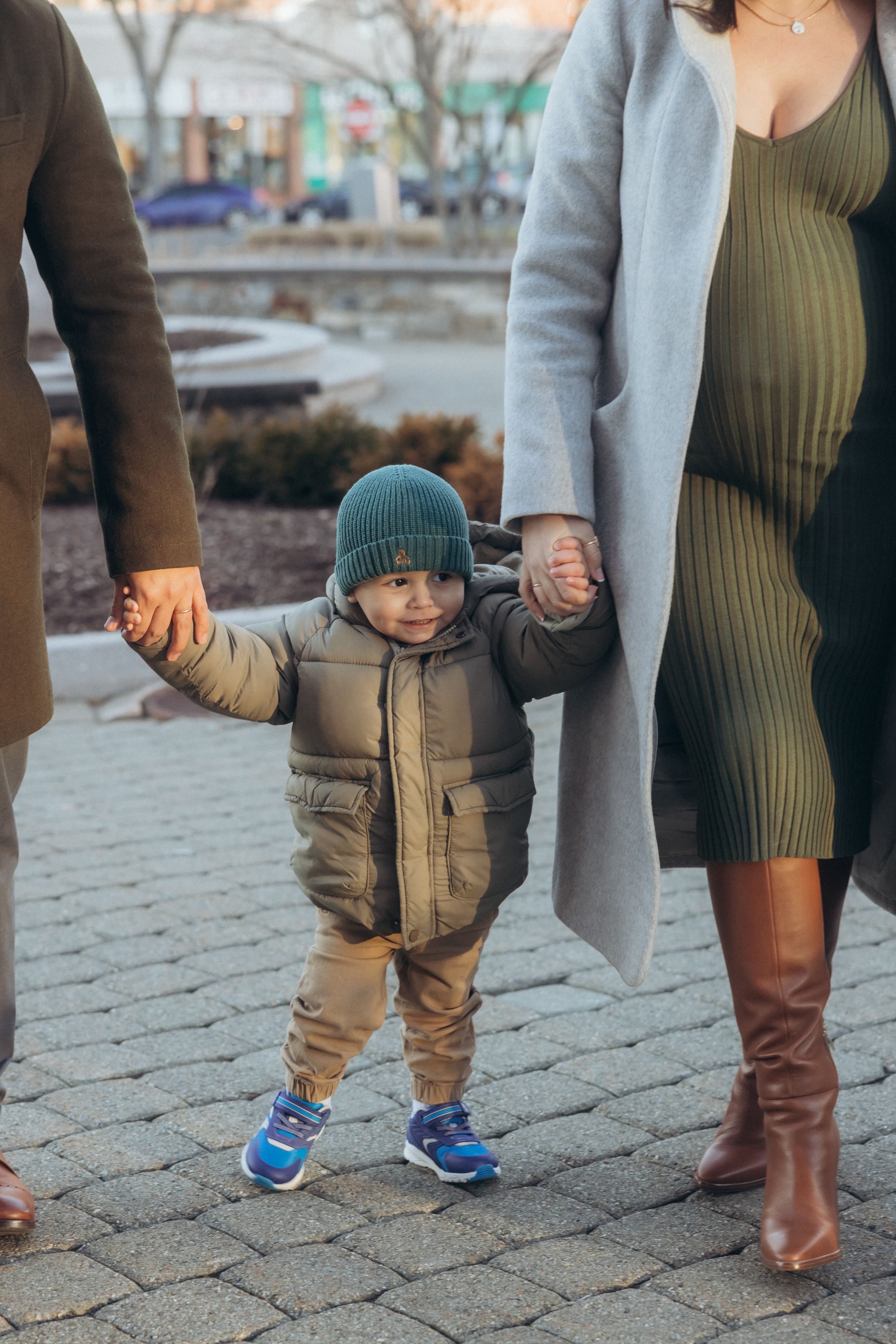 A child holding hands with adults while walking on a cobblestone street.
