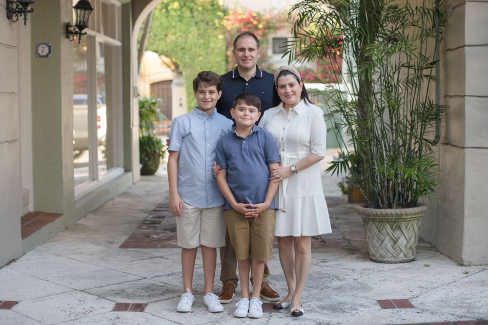 Family portraits captured in an elegant outdoor colonnade with palm trees and stone architecture.