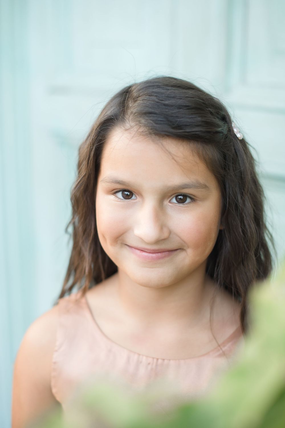 Young person in soft lighting against turquoise background smiling at camera.