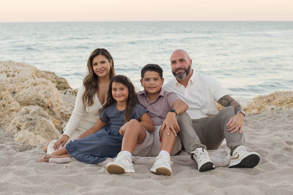 Family relaxing together on rocky beach at sunset with ocean in background.