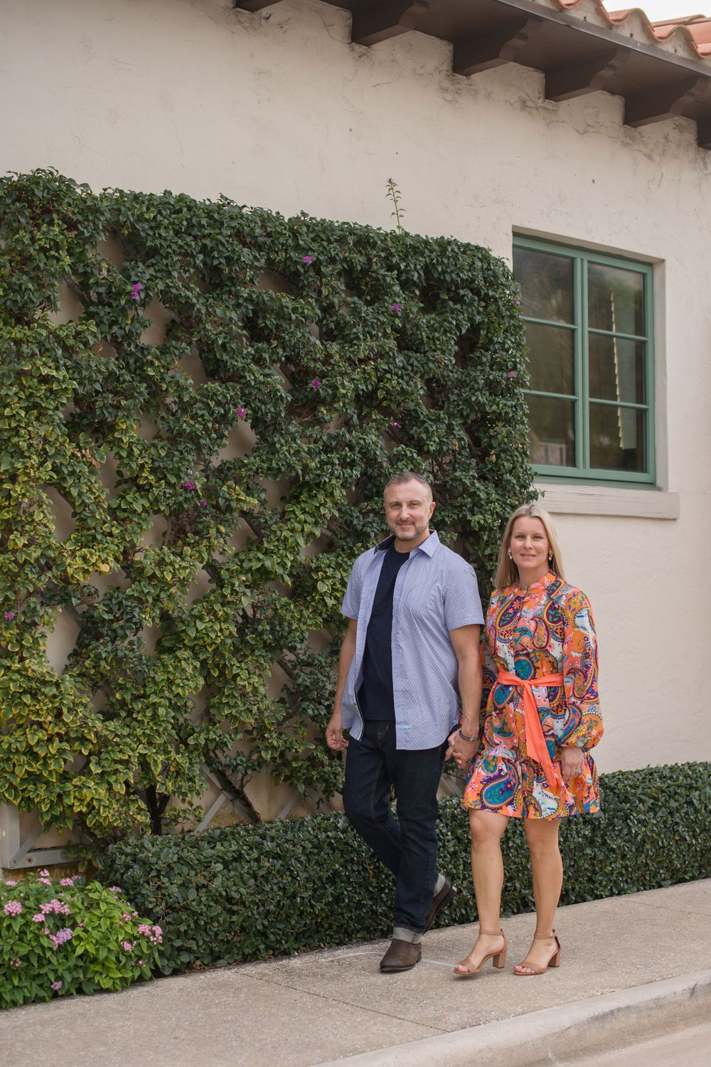Couple standing against a wall covered in lush green ivy and landscaping.