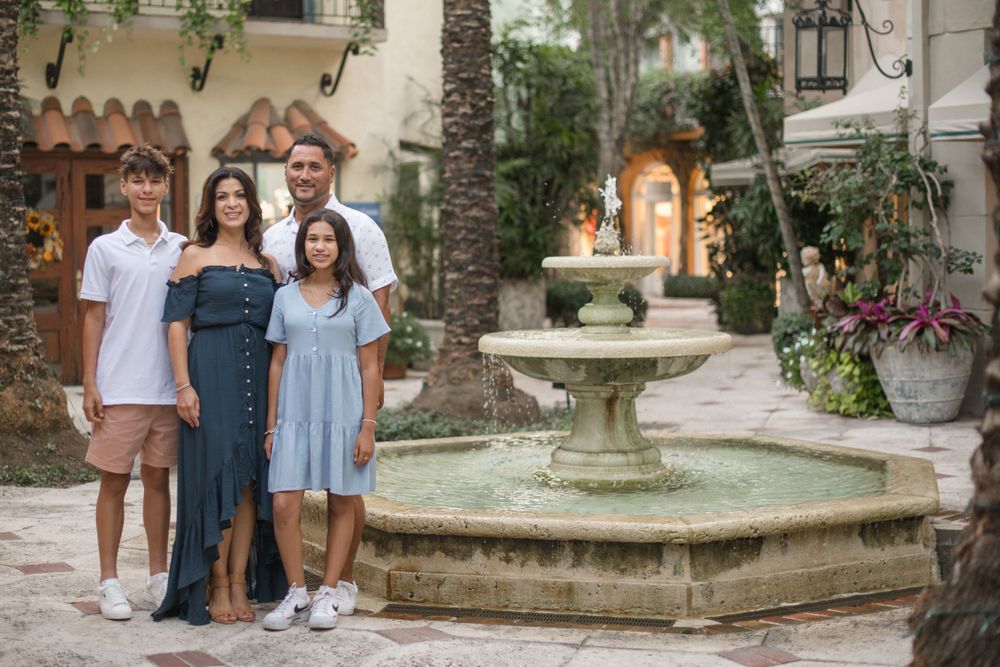 Group posing in front of an ornate stone fountain in a Mediterranean courtyard setting.
