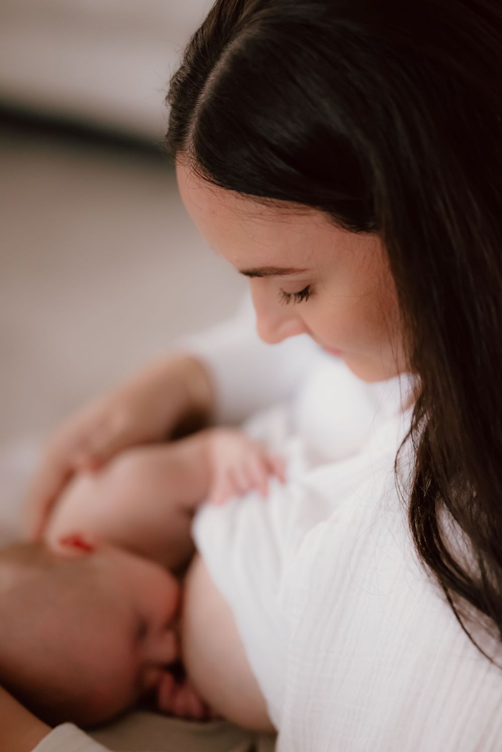 Intimate motherhood moment as mom nurses her newborn baby in soft natural light.