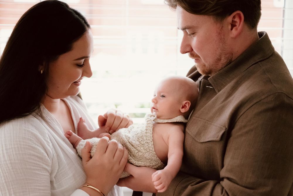 Parents holding and gazing lovingly at their newborn baby in a peaceful indoor setting.