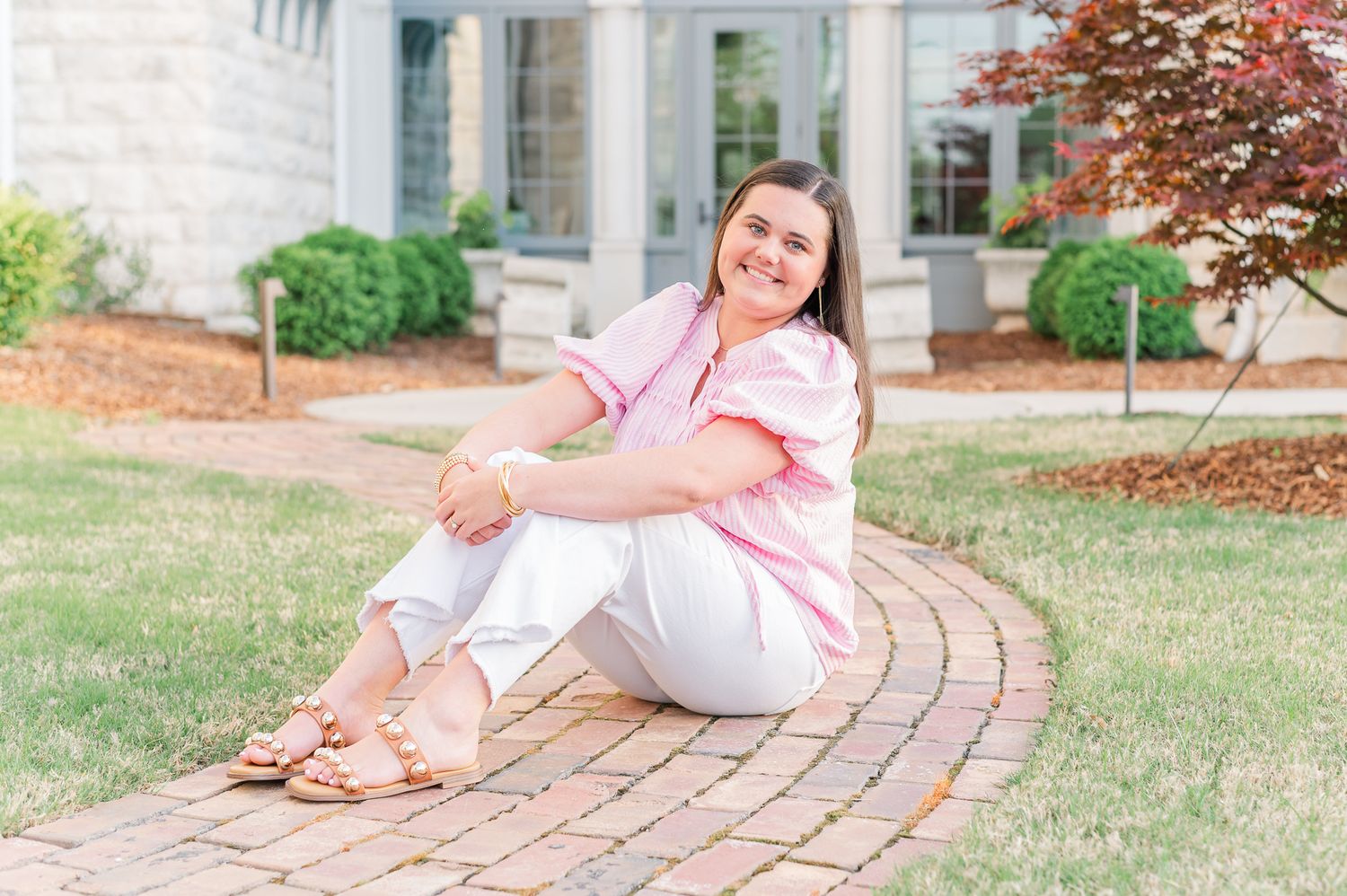 Senior girl sitting on brick path in a yard.
