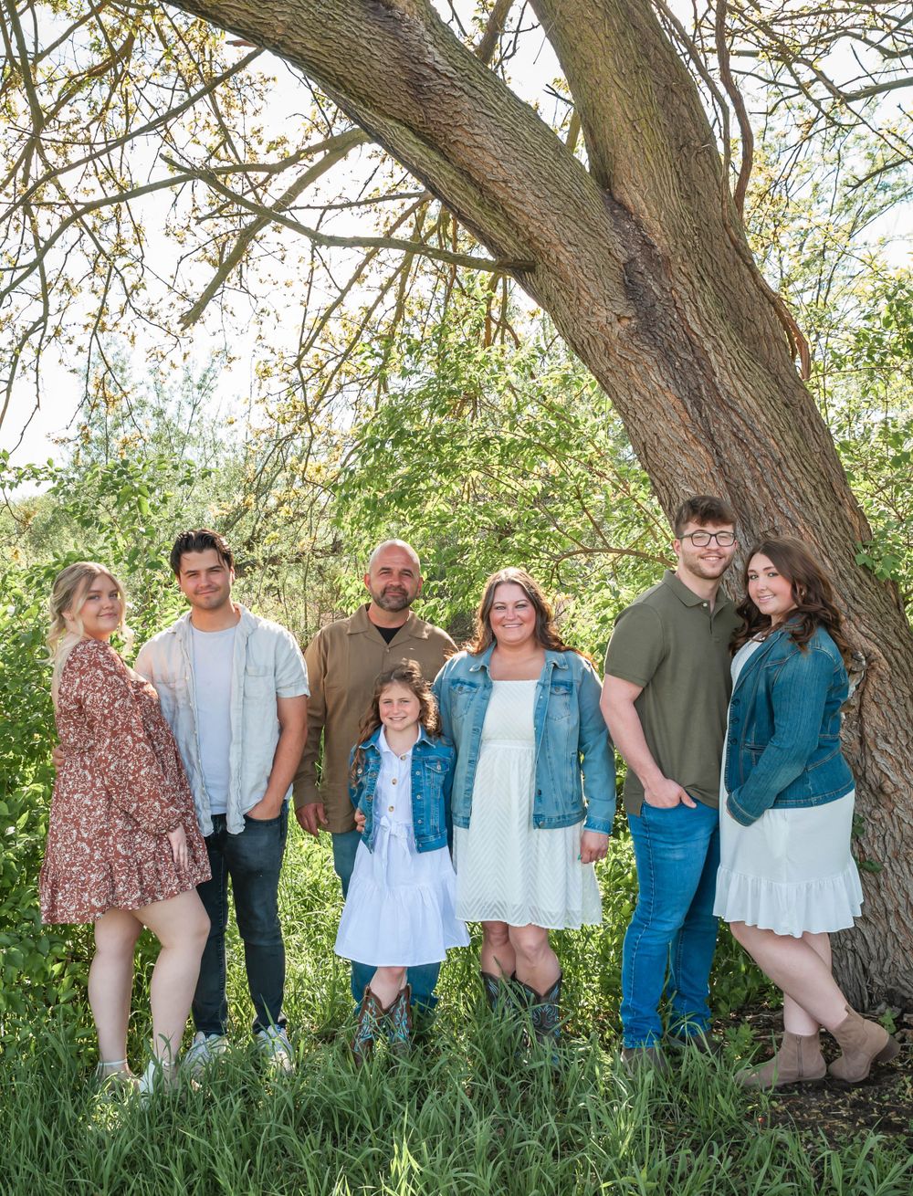 A family group stands under a large tree for a casual outdoor portrait.