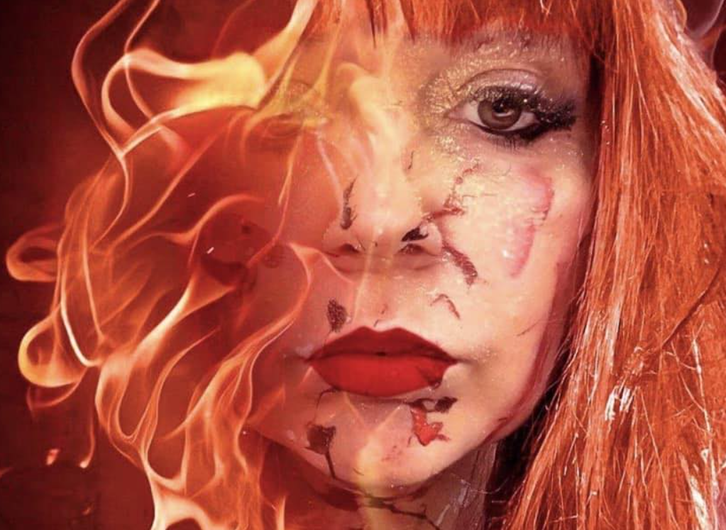 Artistic portrait with vibrant red hair and makeup against dark background with dramatic lighting effects.