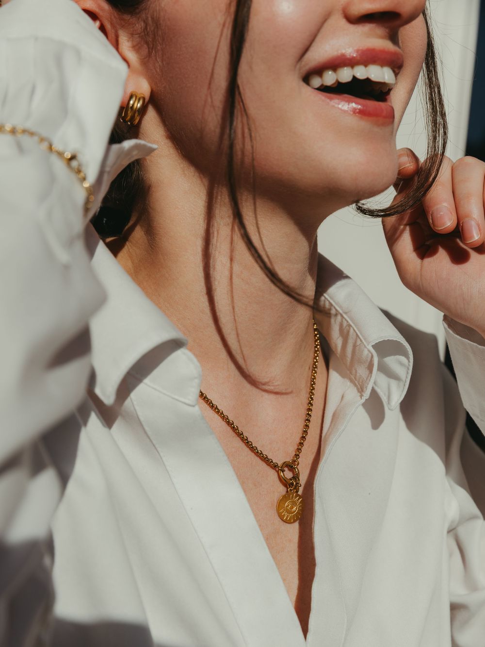 A woman's smile with her hands framing her face, highlighting her gold accessories during branding session.