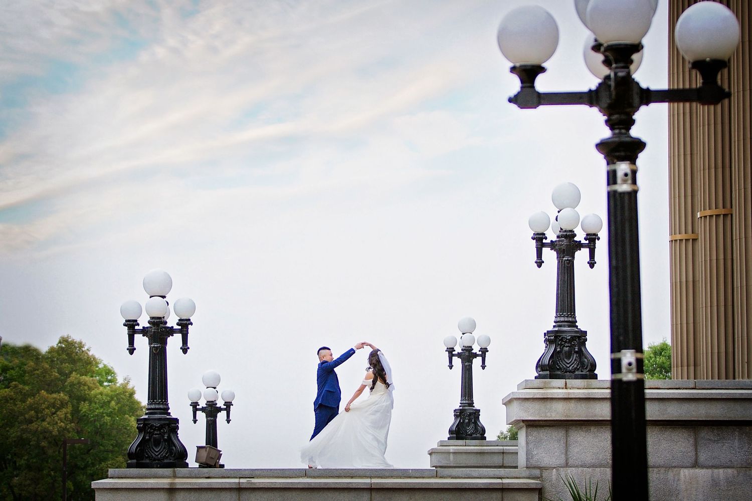 Silhouetted couple dances between ornate vintage street lamps at dusk.