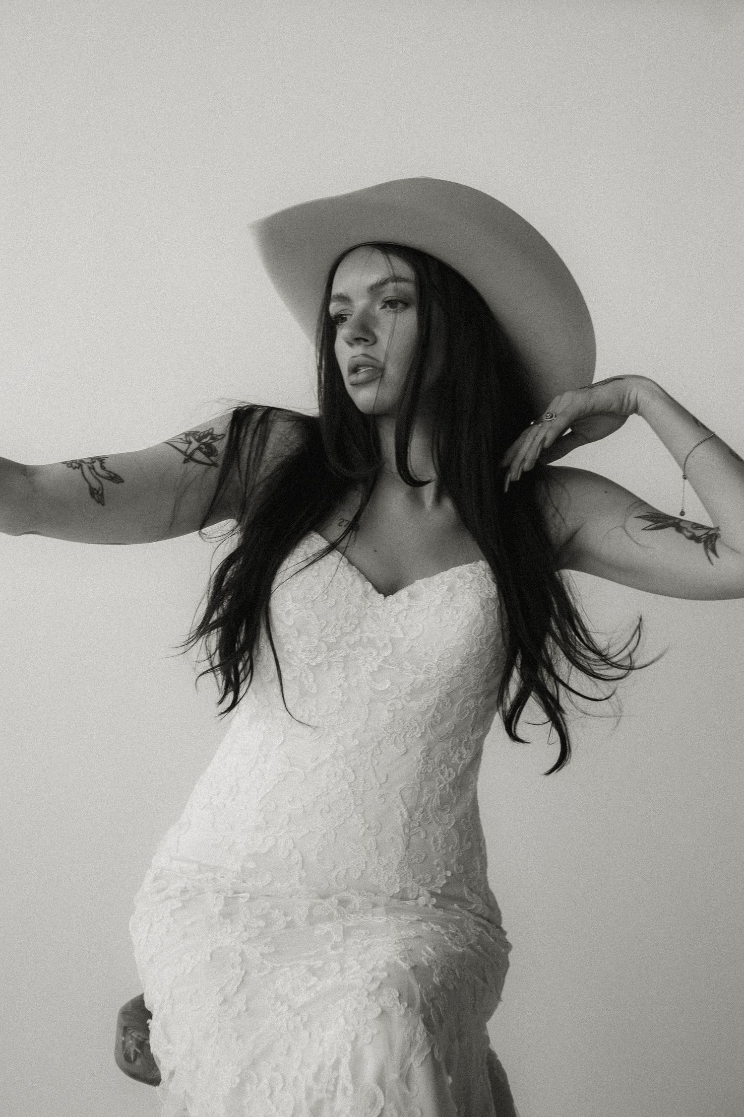 Dramatic black and white bridal portrait featuring lace dress and western hat.