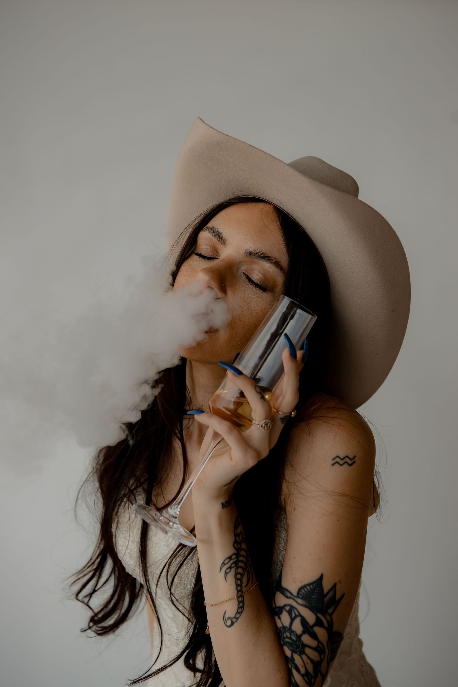 Edgy bridal portrait with cowboy hat and vapor smoke against minimal background.