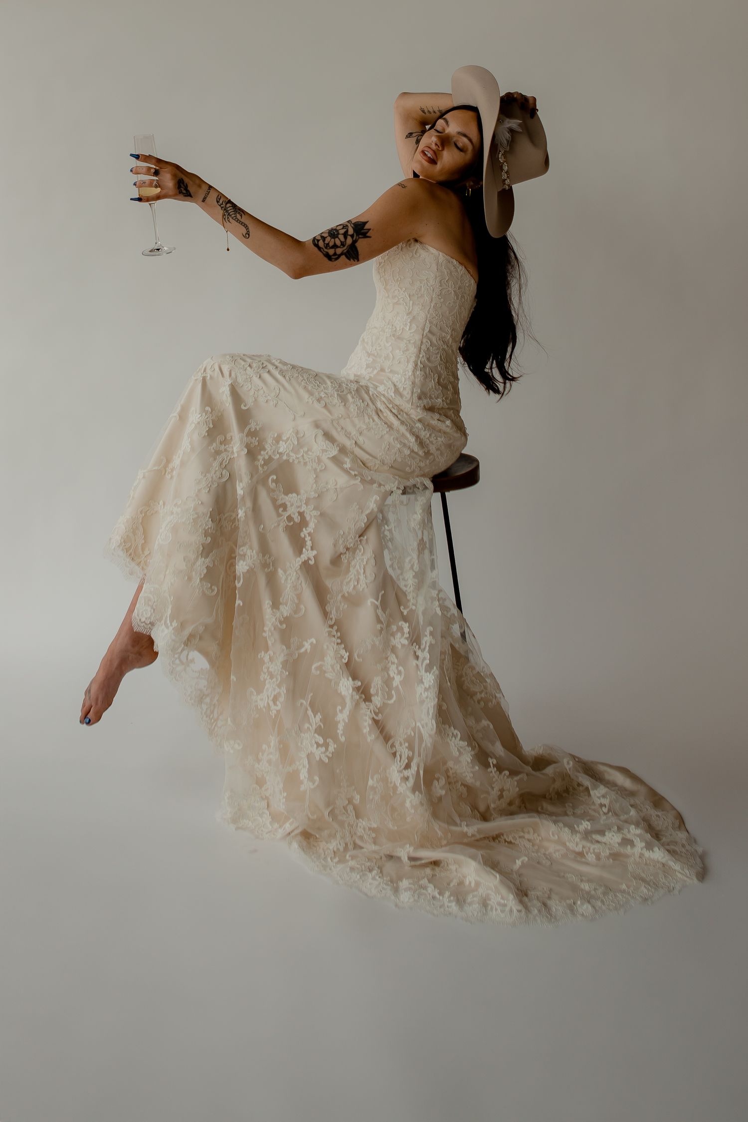 A playful bride in a lace wedding dress and cowboy hat poses dynamically against a white background.
