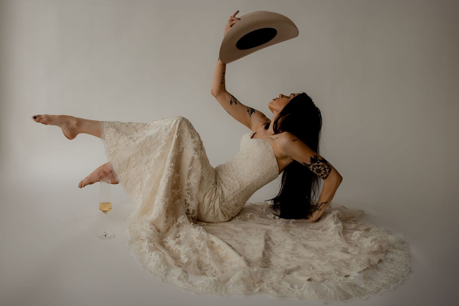 A dynamic bridal pose showcasing a flowing lace dress and western hat against white.