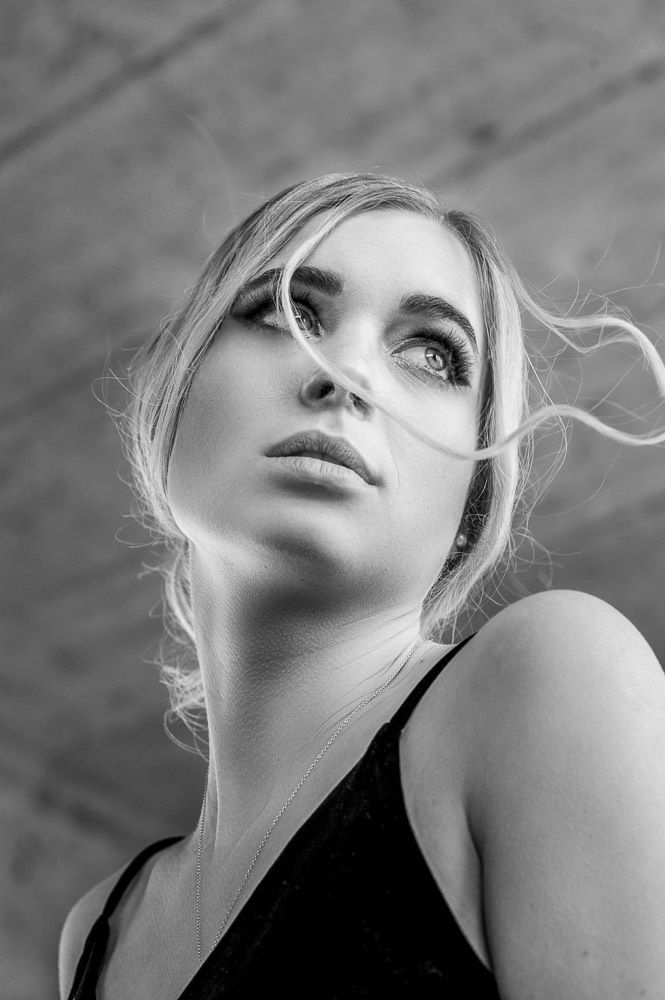 Black and white close-up portrait of a blonde woman gazing upward with wispy hair.