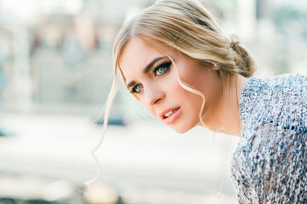 Close-up portrait of a blonde woman with blue eyes and natural makeup in a knit sweater.