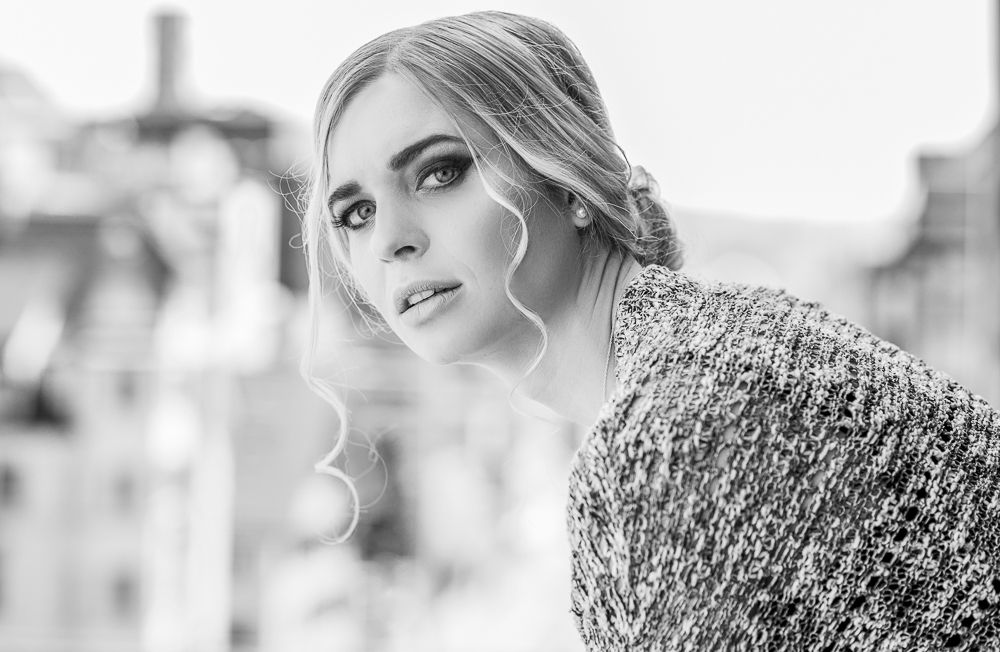 Black and white portrait of a blonde woman with elegant updo and knit sweater in urban setting.