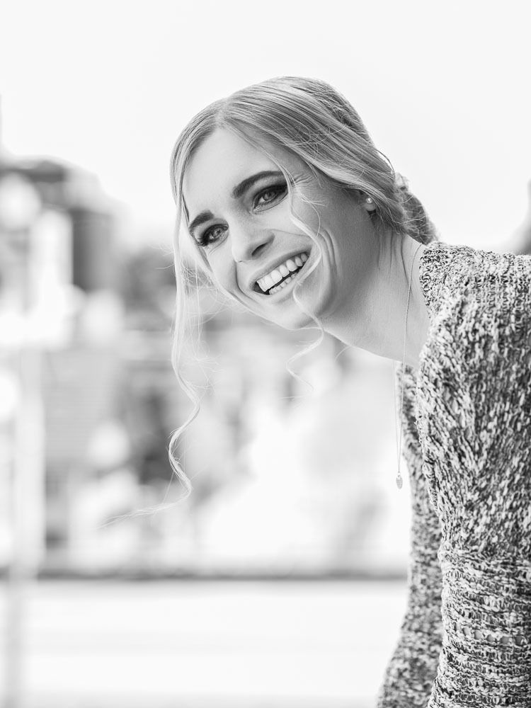 Black and white photo of a smiling blonde woman with updo hairstyle in a knit dress outdoors.