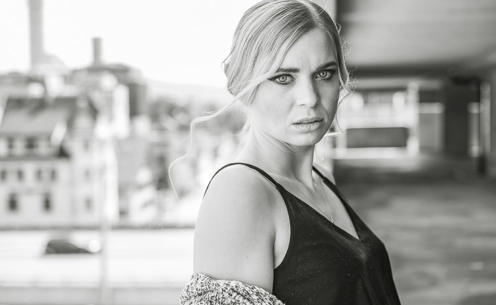 Black and white portrait of a blonde woman in a black dress with knit cardigan in urban setting.