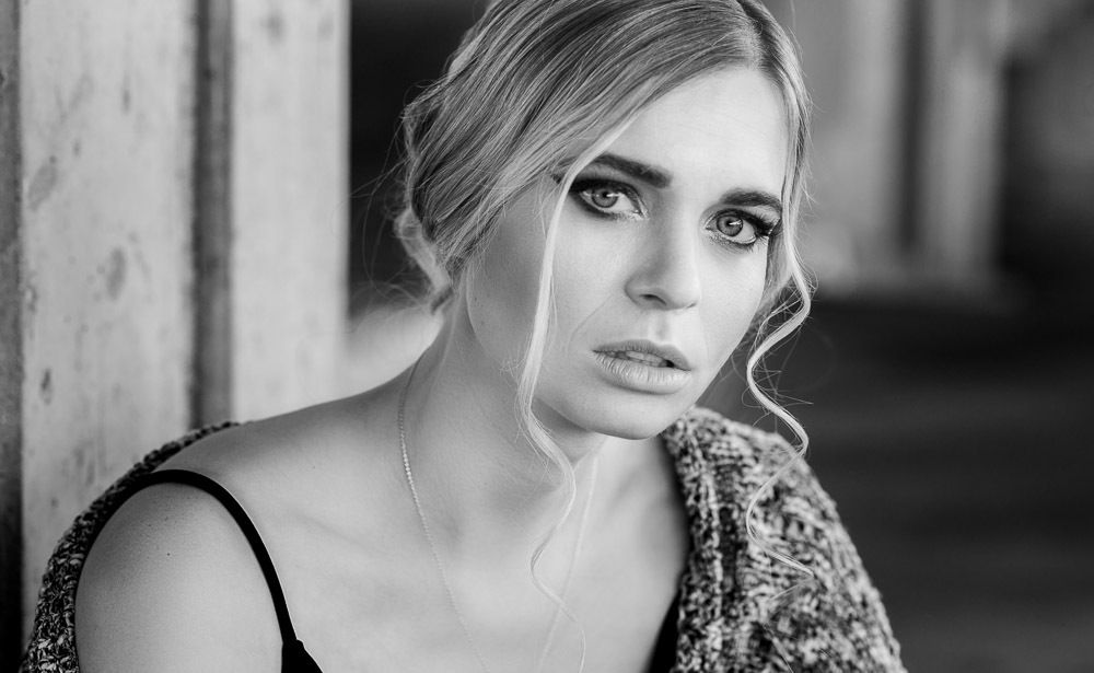 Black and white portrait of a blonde woman with elegant updo and smoky eye makeup.