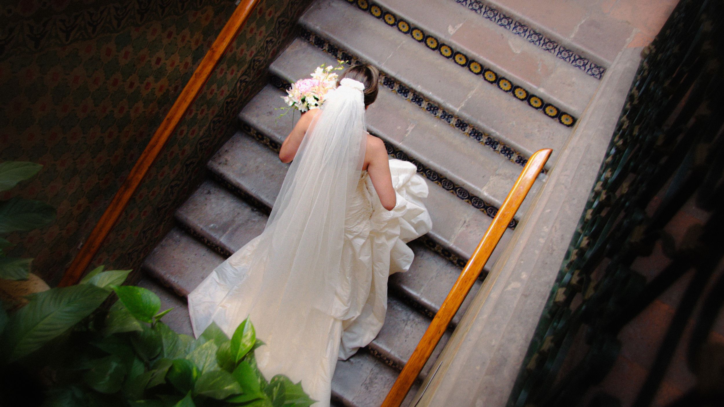 Bride in flowing white gown descending ornate staircase.