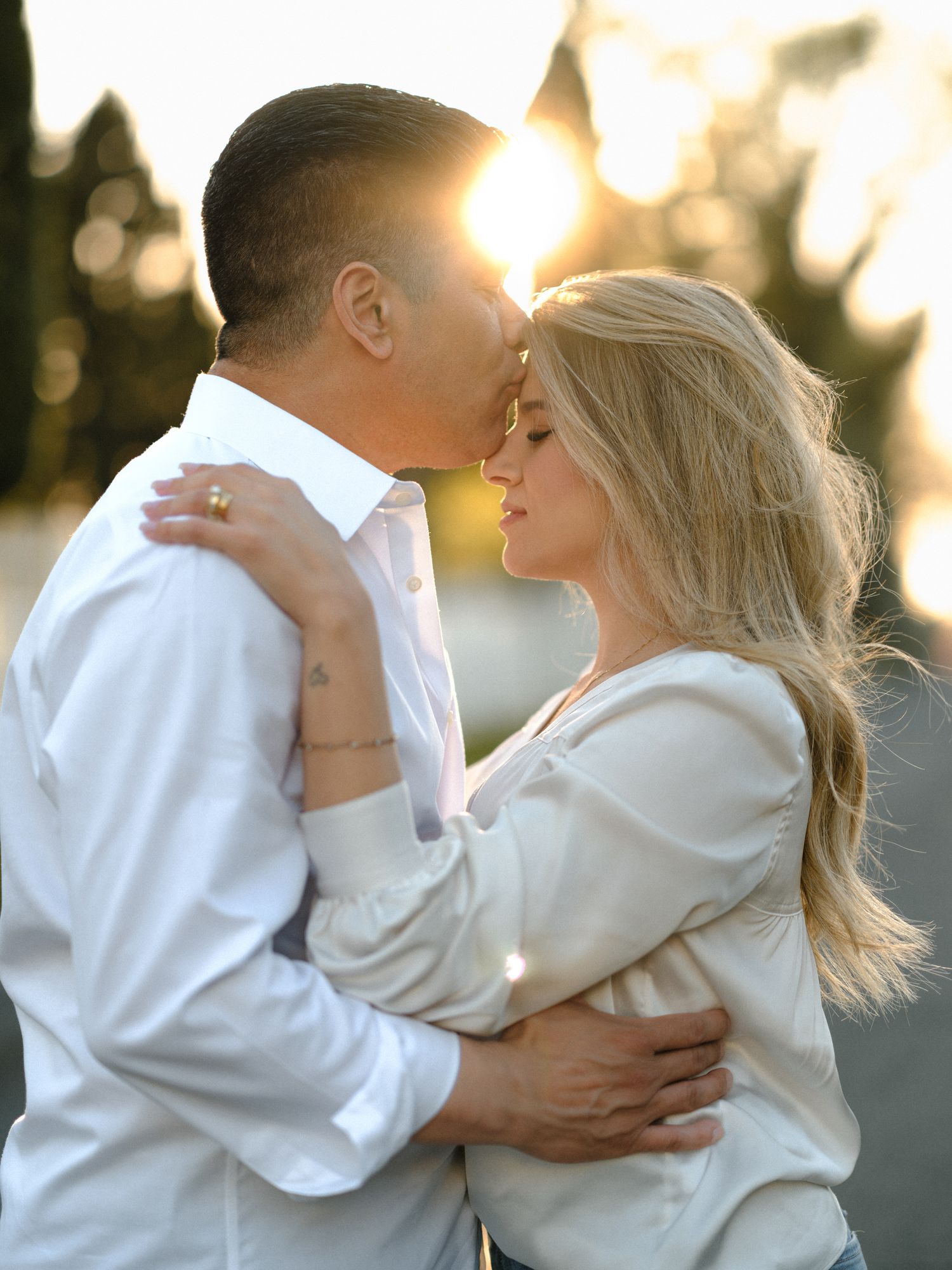 Romantic embrace captured during golden hour with sunlight creating a warm glow.
