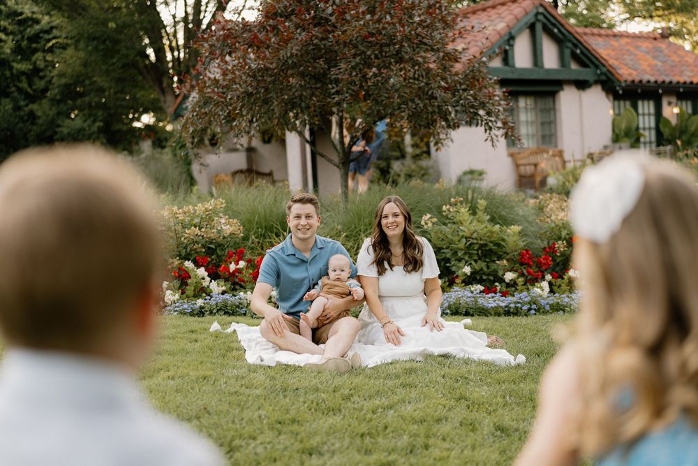 Two people sitting together on a white blanket in a garden during an outdoor photo session.