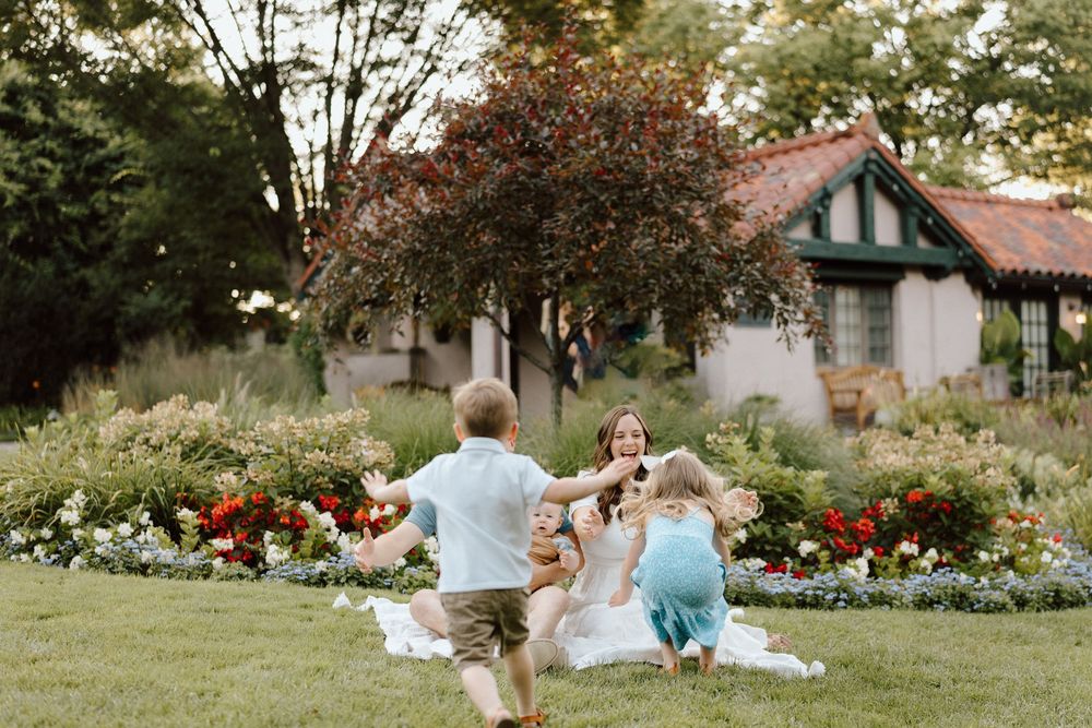 Two people sit together on a blanket in a garden surrounded by colorful blooms and trees in summer.