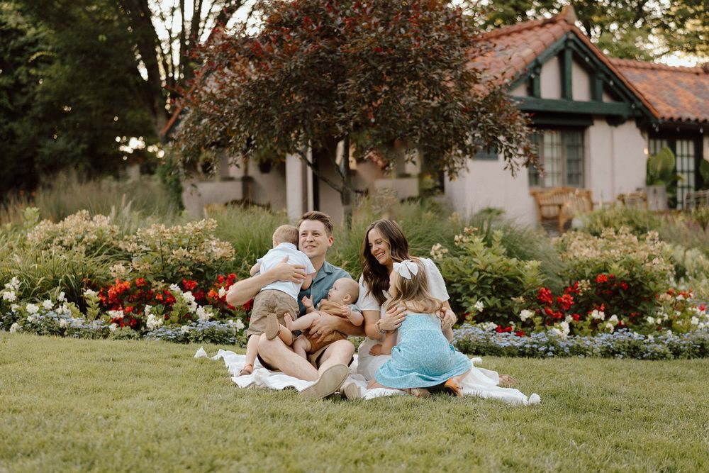People enjoying a relaxing summer day while lounging on a grassy lawn near a garden with colorful flowers.