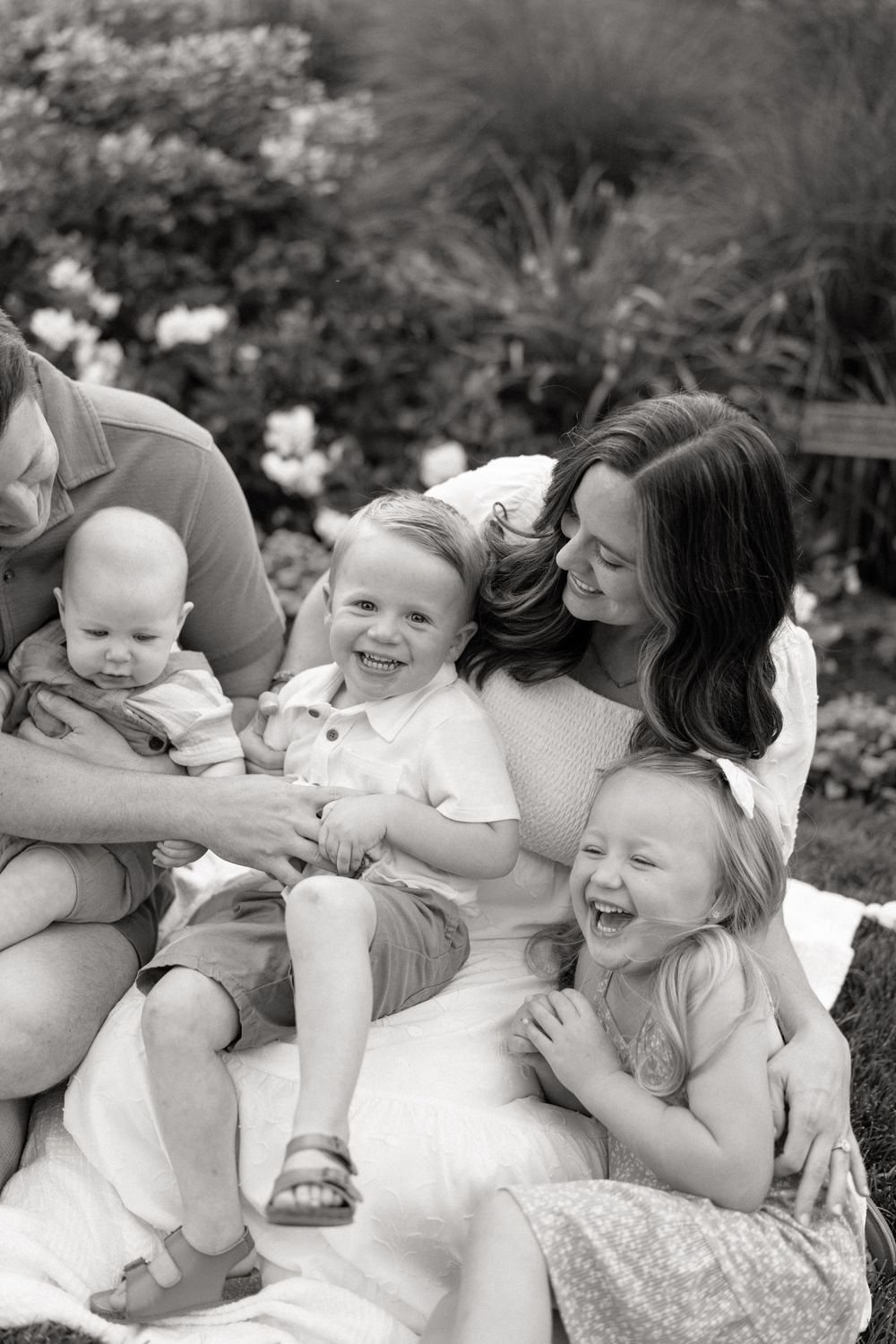 A candid black and white photo captures joyful family moments in a garden setting with children laughing and playing.