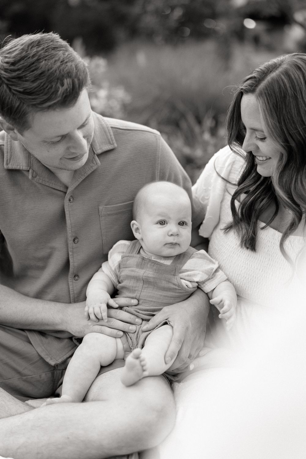 Black and white family portrait series showing tender moments with a baby in a garden setting.