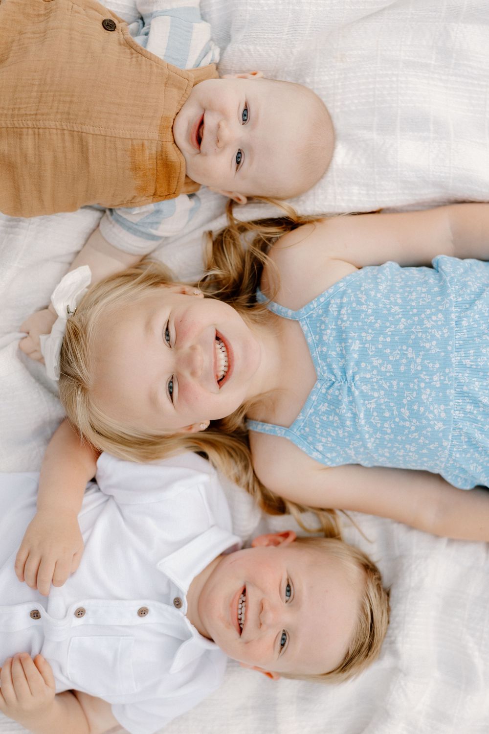 Two children lying on white bedding share joyful laughs together.