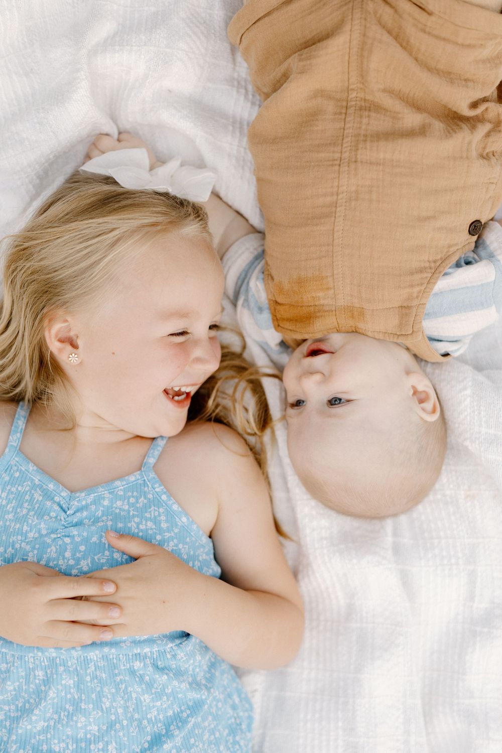Several close-up shots showing joyful interaction between siblings laid on white blanket.