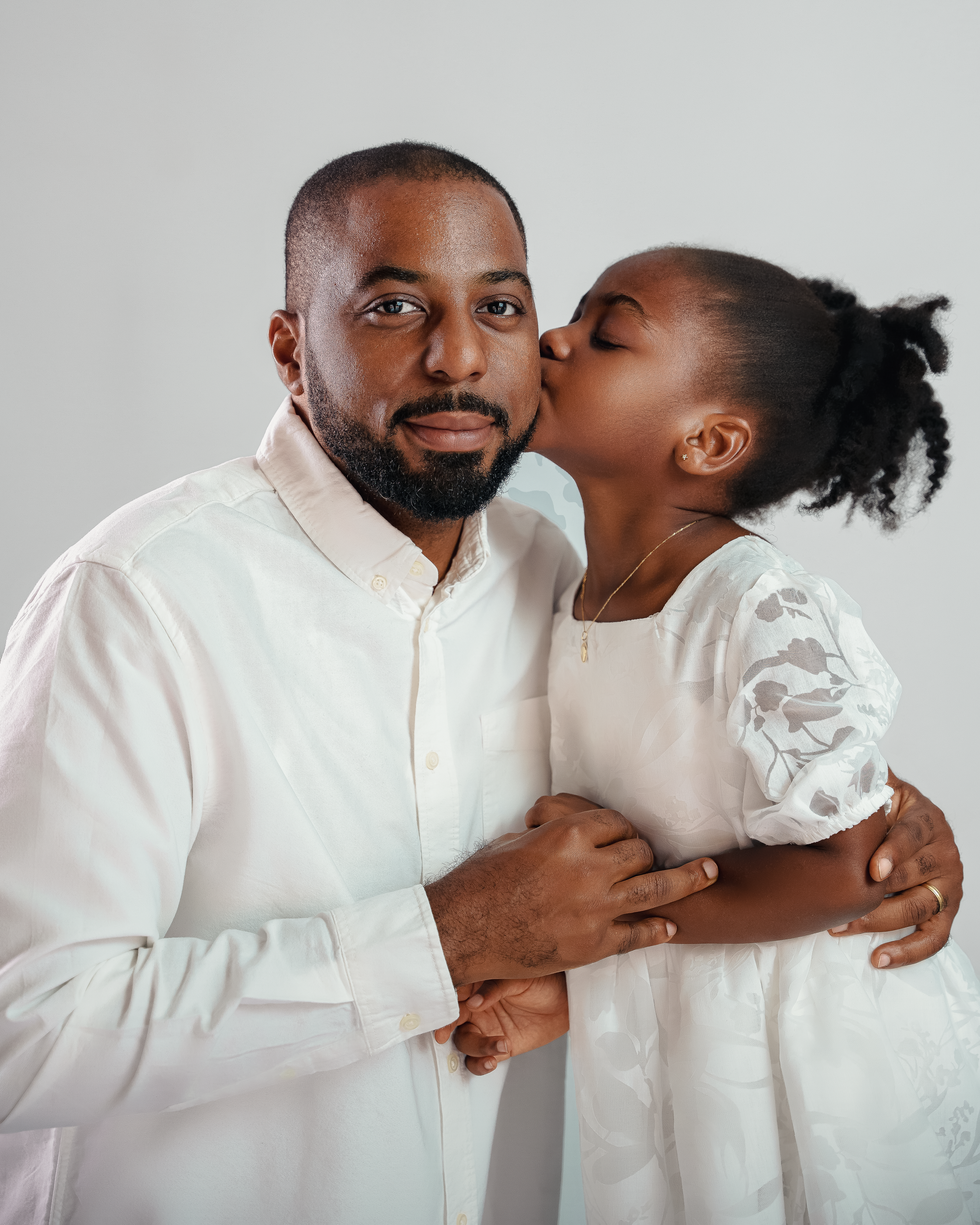 Sweet moment between parent and child both wearing white during family photoshoot.