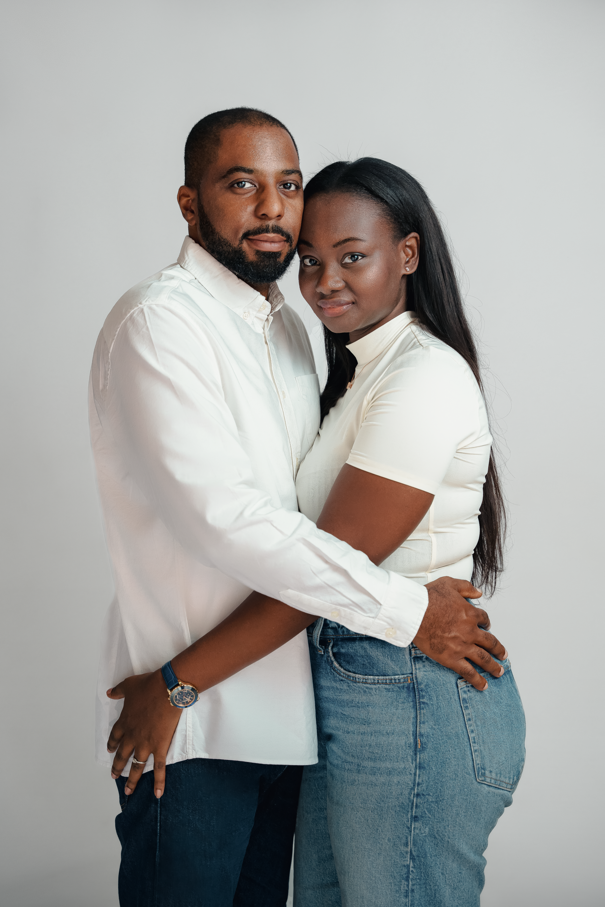 Studio portrait of a couple in white shirts embracing against a light gray background.