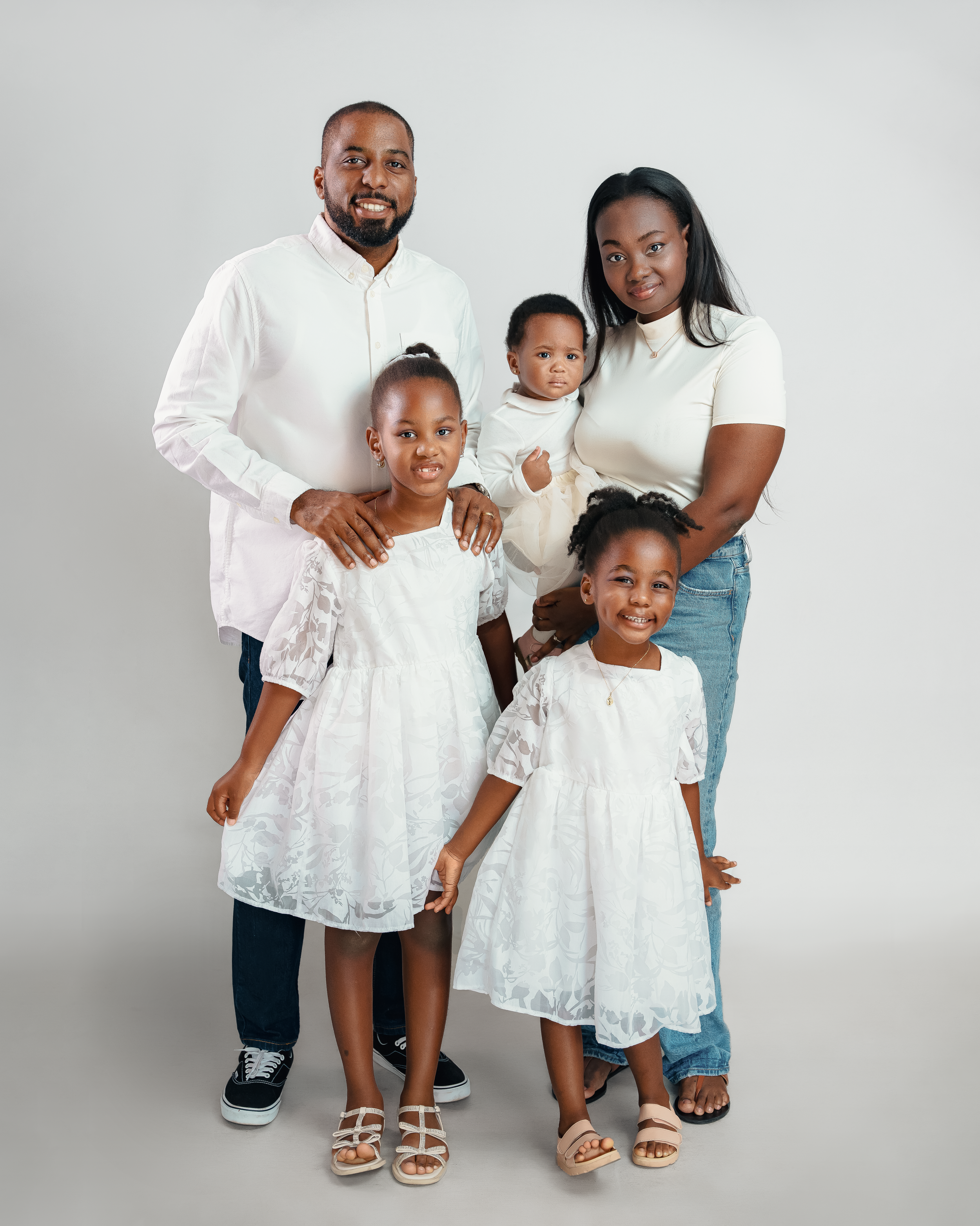 Family portrait of parents and three children all wearing coordinated white and neutral outfits.