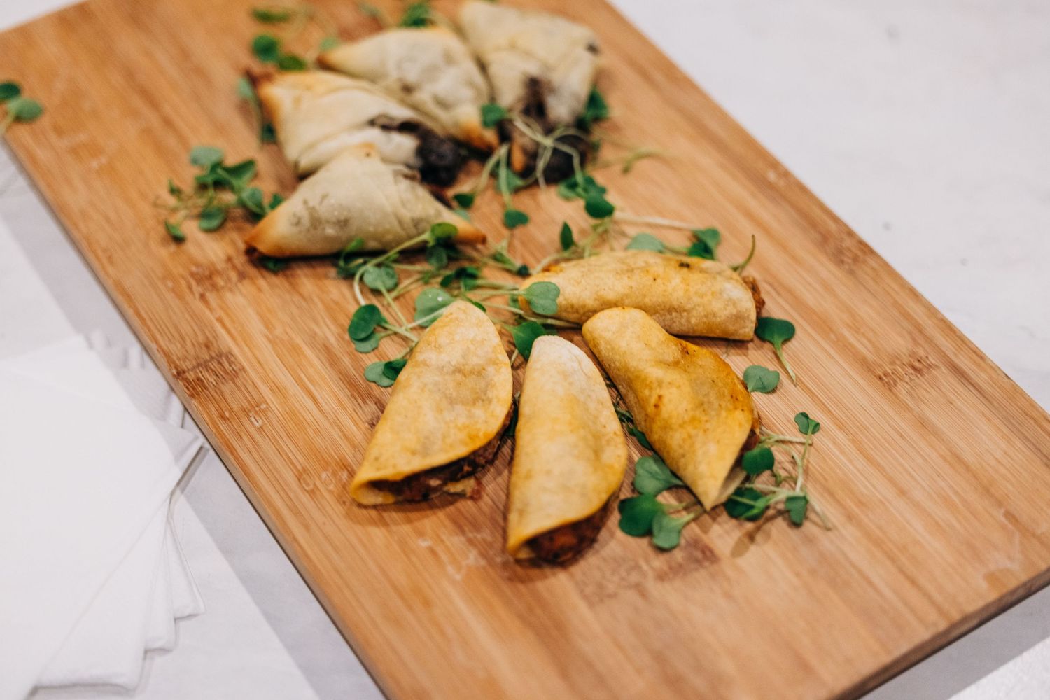 Golden samosas garnished with fresh herbs served on a wooden cutting board.