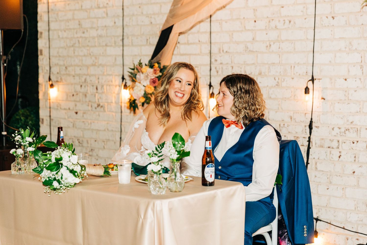 Couple sharing drinks and conversation at decorated wedding reception table.