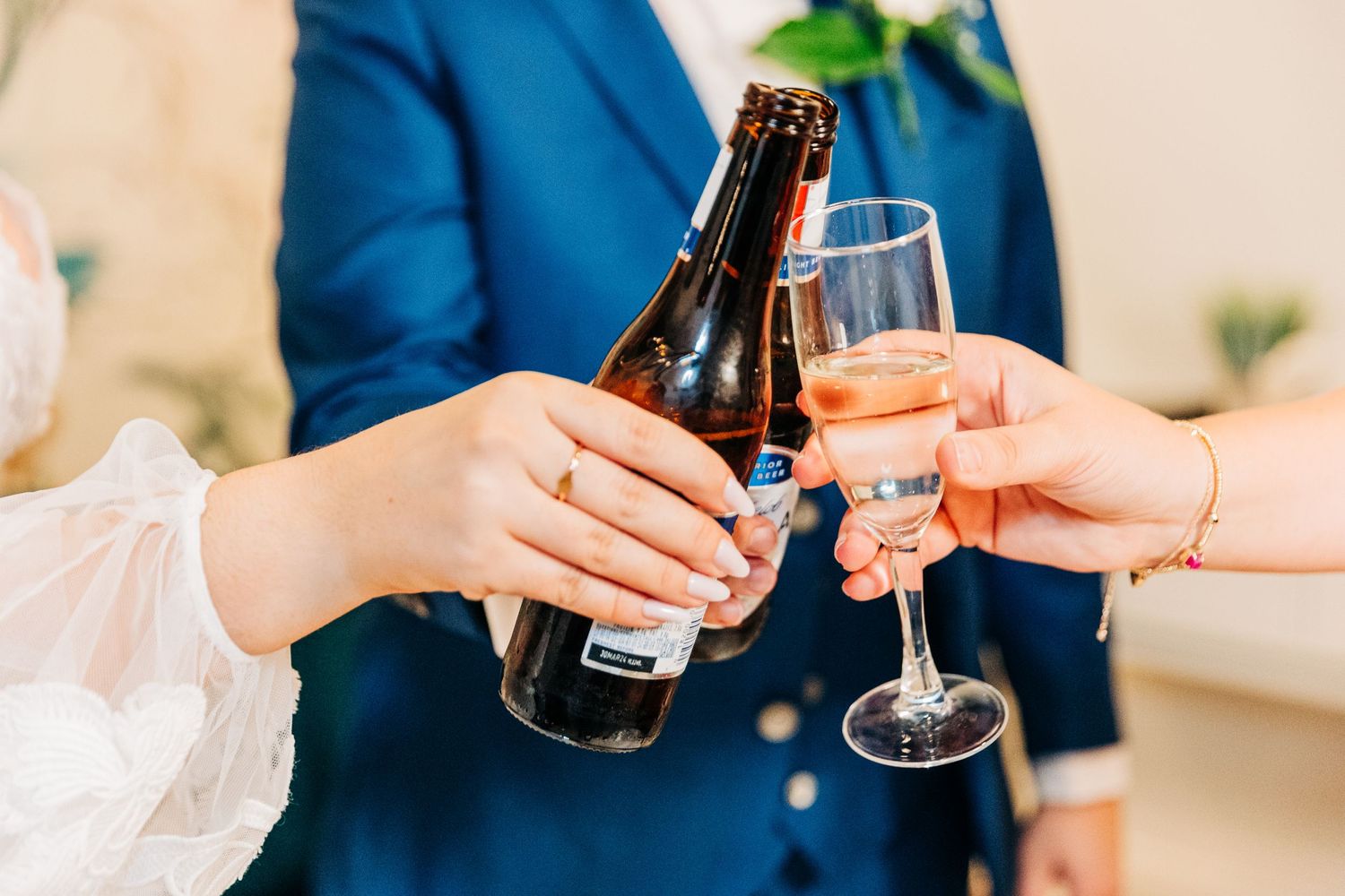 Hands toasting with champagne glass and beer bottle at celebration.
