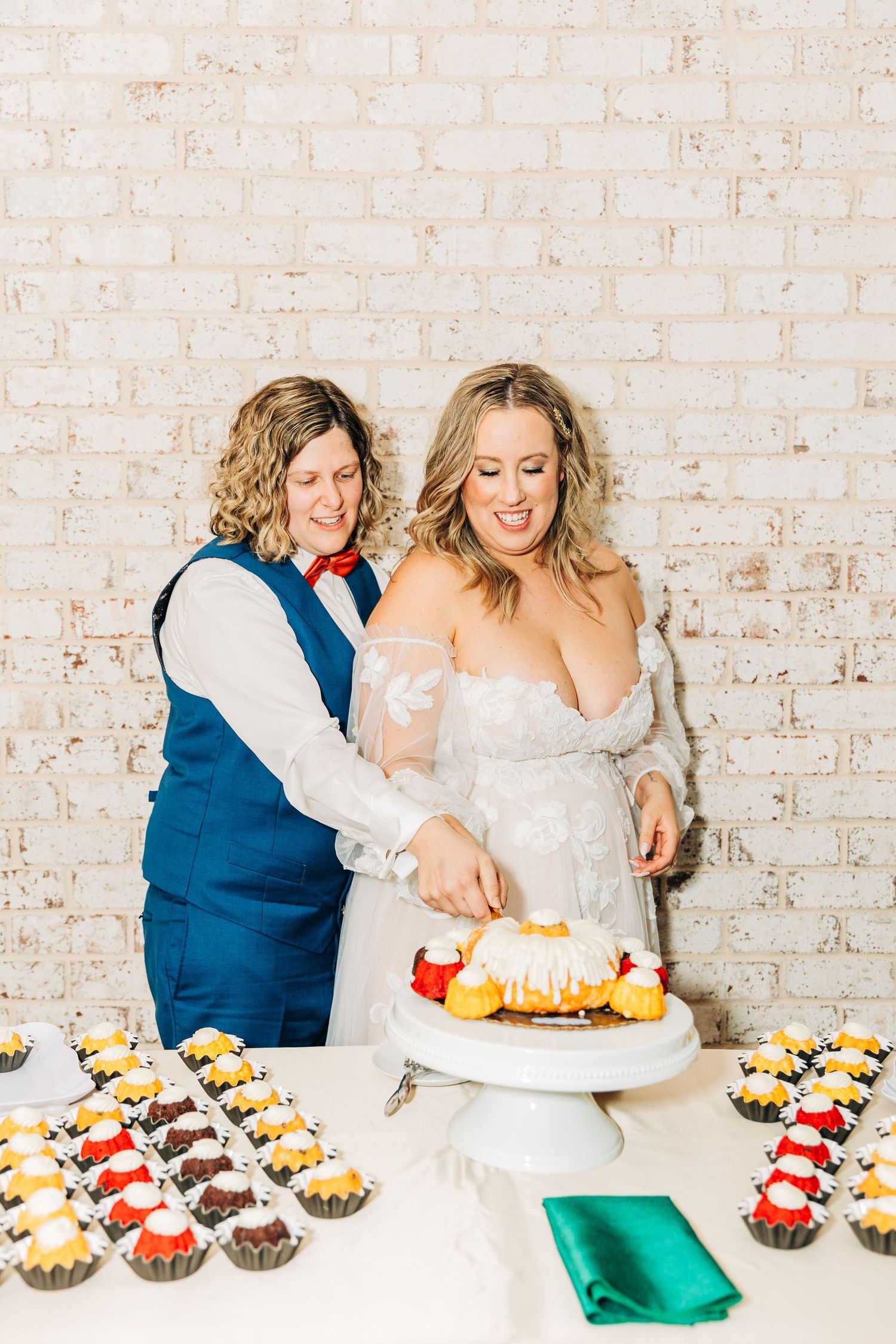 Couple cutting wedding cake together at dessert table with cupcakes.