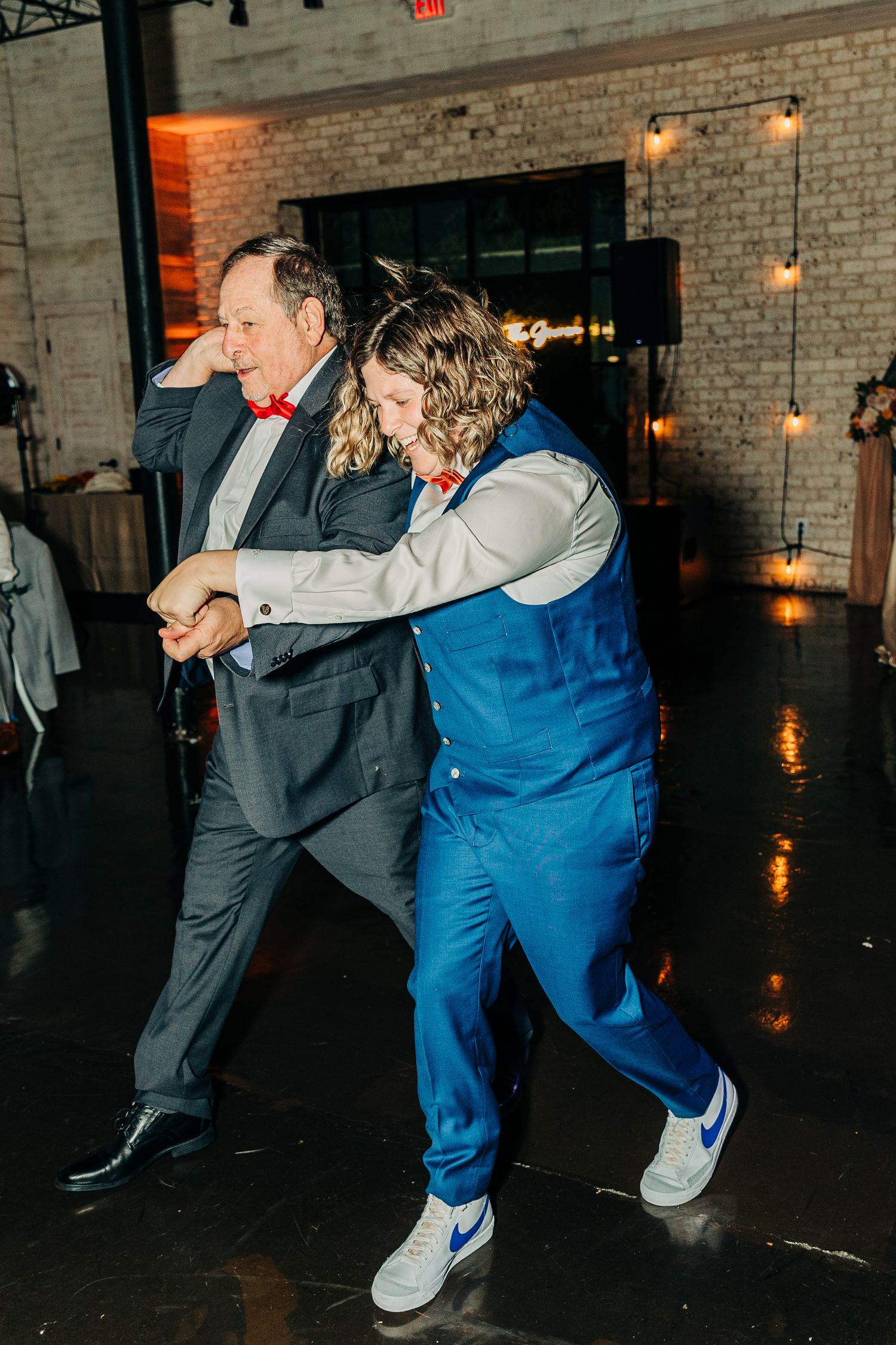 Two wedding guests dance energetically together on the reception dance floor in formal attire.