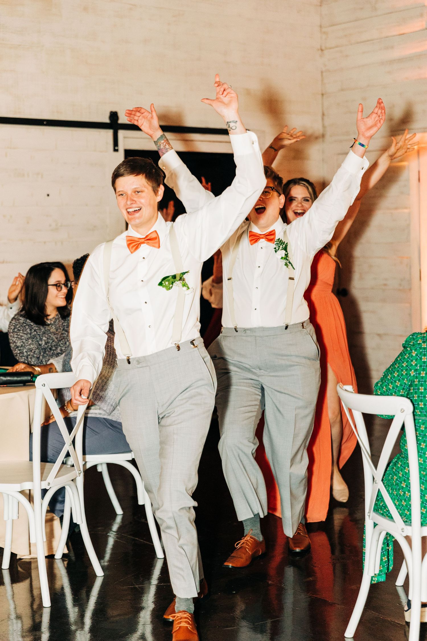Wedding guests in suspenders and bowties dancing enthusiastically at reception.