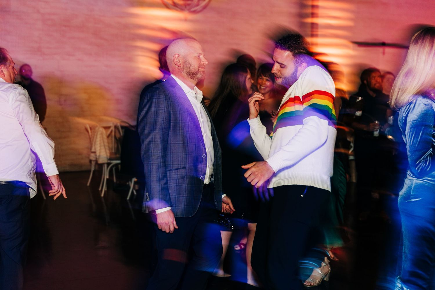 Wedding guests dance and celebrate in a dimly lit venue with brick walls.