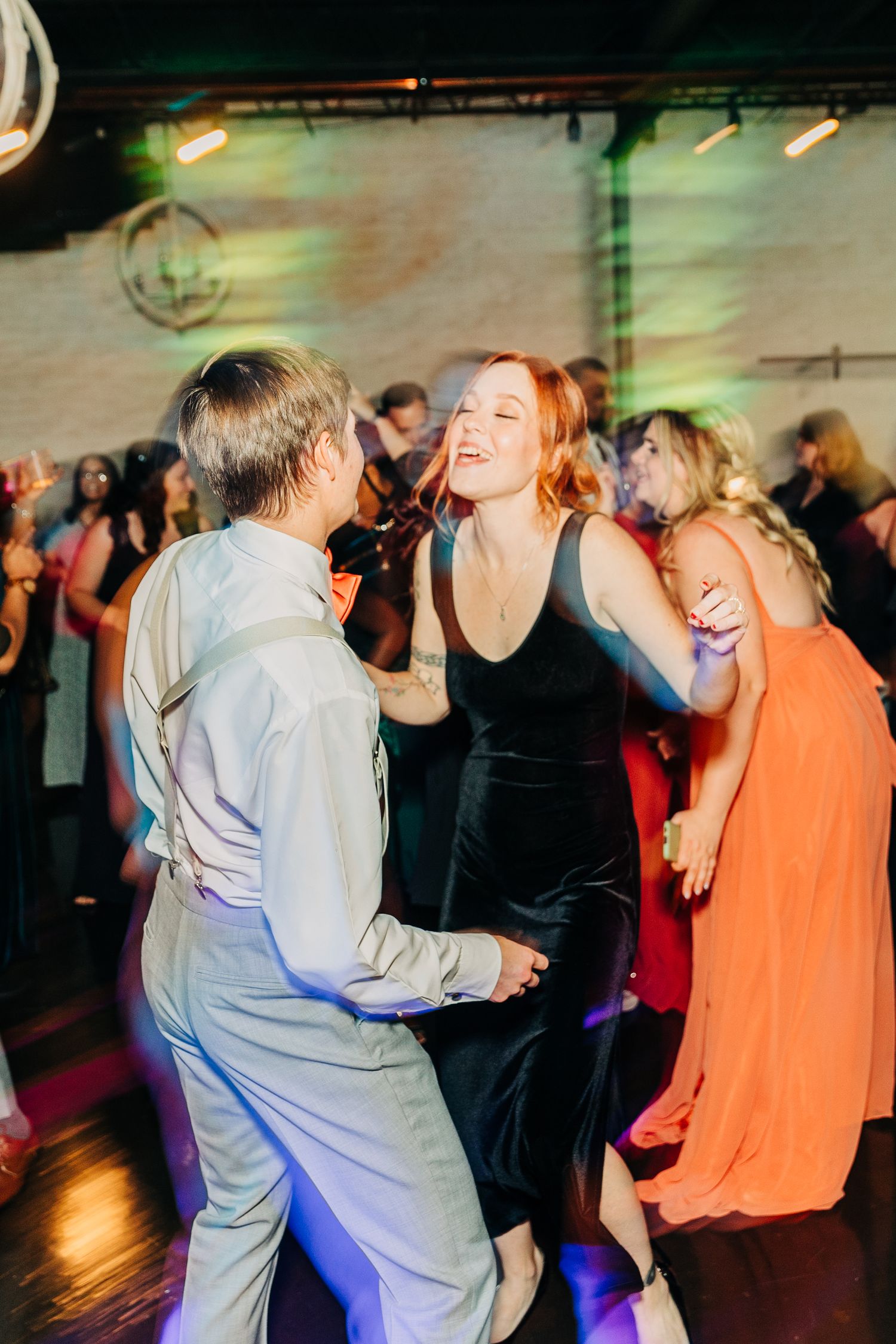 Couples dance together at a wedding reception with mood lighting and brick walls.