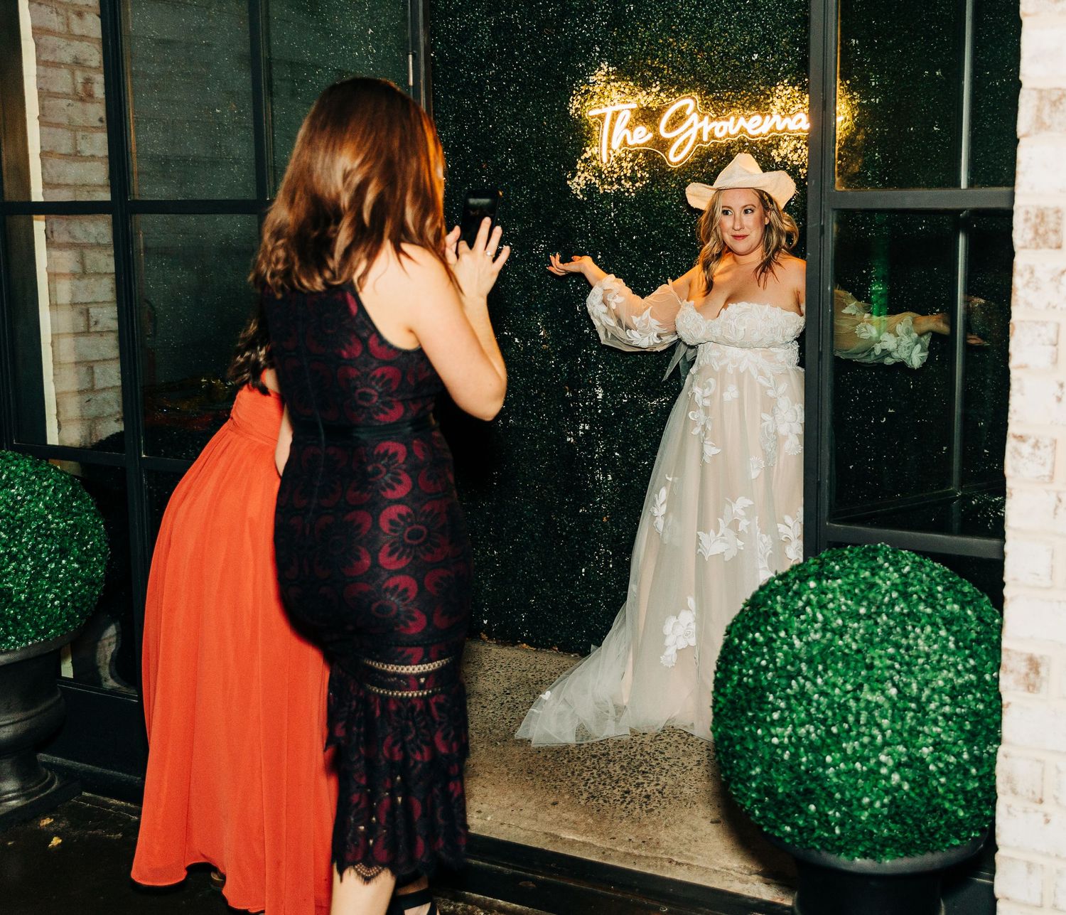 Two guests pose in front of an illuminated neon sign at a wedding.