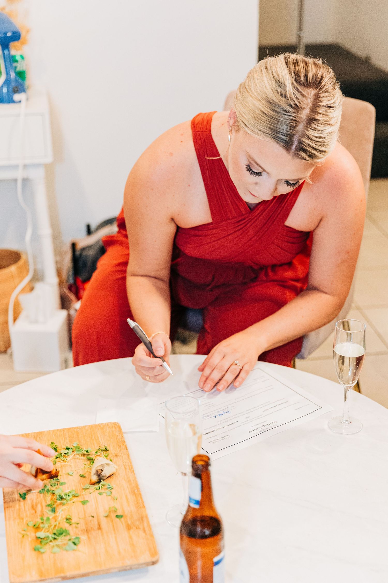 Person in red dress writing notes at table with food and drinks.