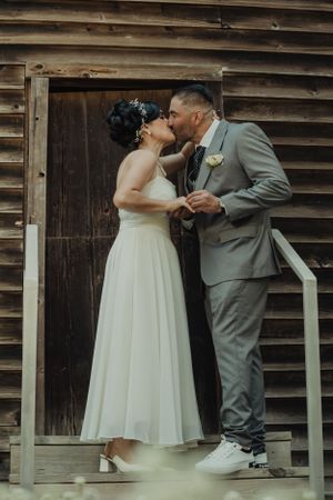 Newlyweds share intimate moment against rustic wooden backdrop.